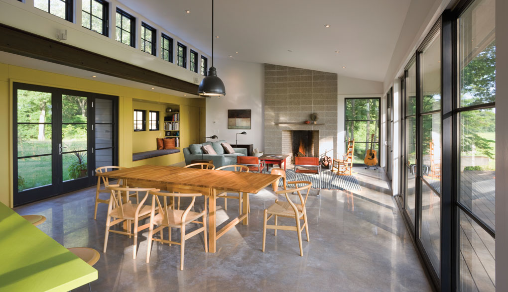 A large open living room shows a dining table in the foreground, and in the background is a fireplace surrounded by a coffee table, sofa and chairs.