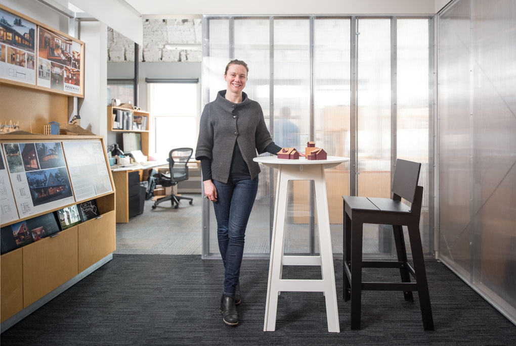 Jody McGuire stands next to white table with a model homes place on top of it in the middle of an office.