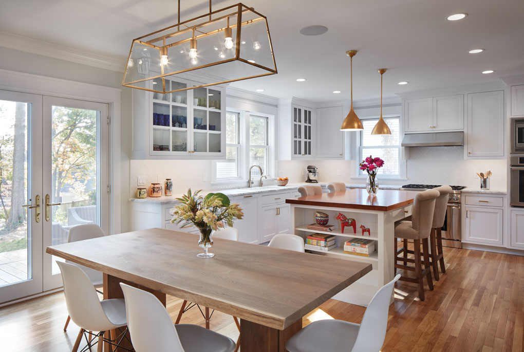 A remodeled kitchen gives a modern feel and features hardwood flooring, white cabinetry, and a wrought-iron chandelier of the dining table.