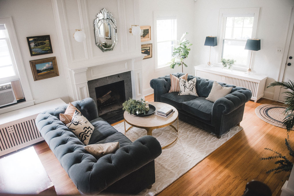 A living room designed by Victoria Sass shows Chesterfield-style sofas flanking a coffee table that is set next to a fireplace.