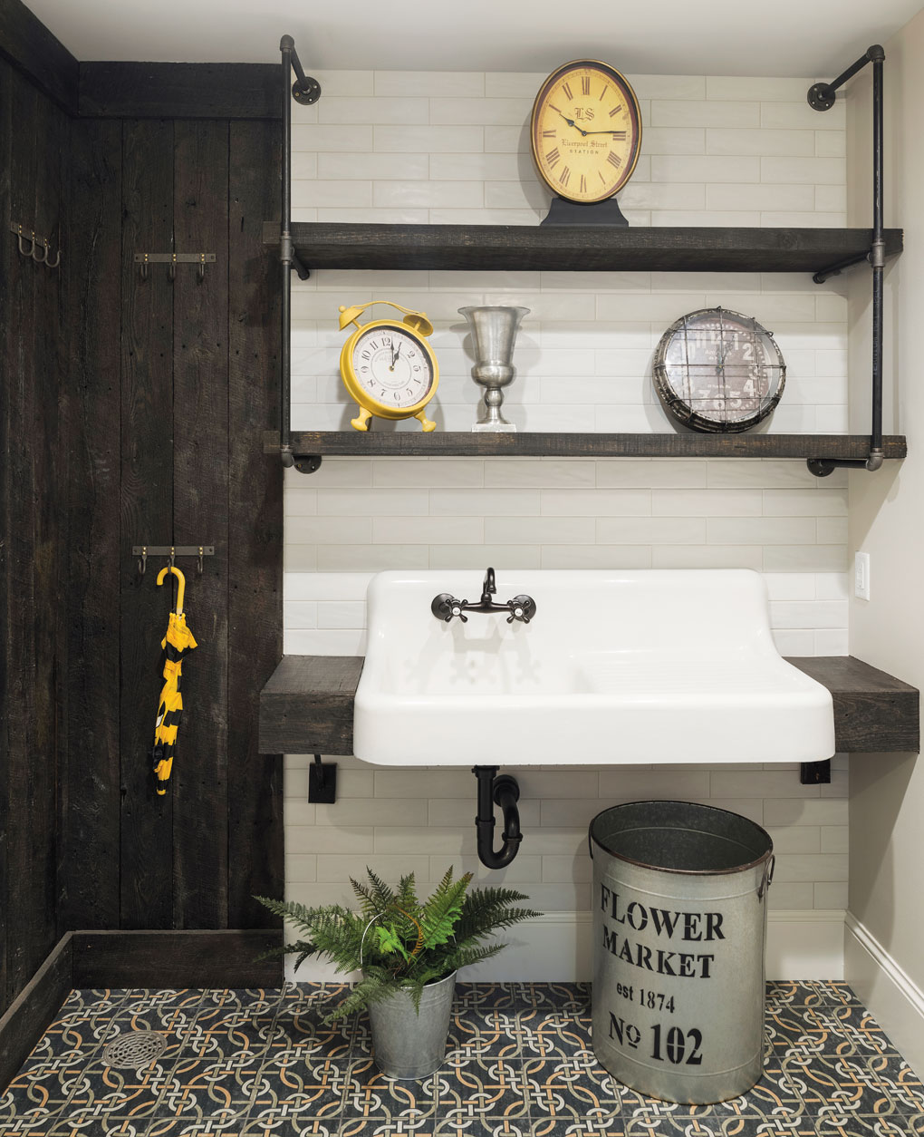 A mudroom with three clocks adorning the shelves above a large sink. An umbrella hangs on a nearby wall.
