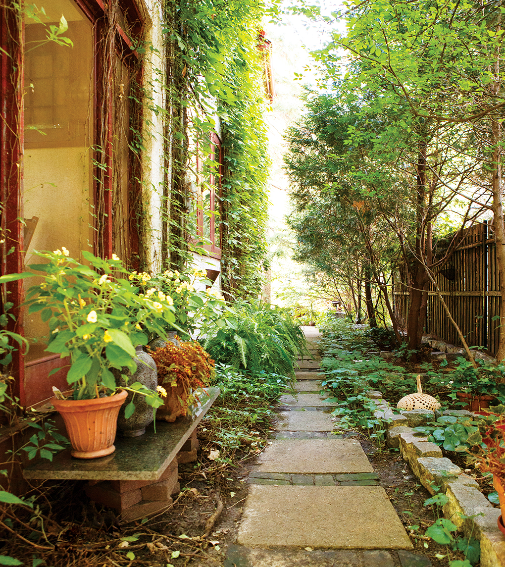 Pots and plants line a stone walkway leading to the back of a home.