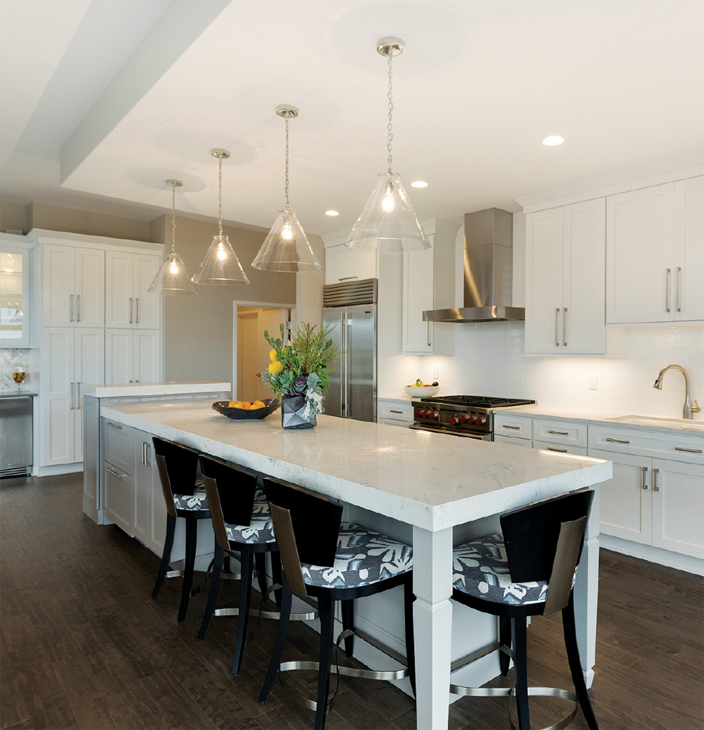 A kitchen with all white cabinetry, stainless steel appliances, center island with surrounding stools and dark, hardwood flooring by Ispiri Design-Build, a winner of the National Kitchen and Bath Association Minnesota Design Awards.