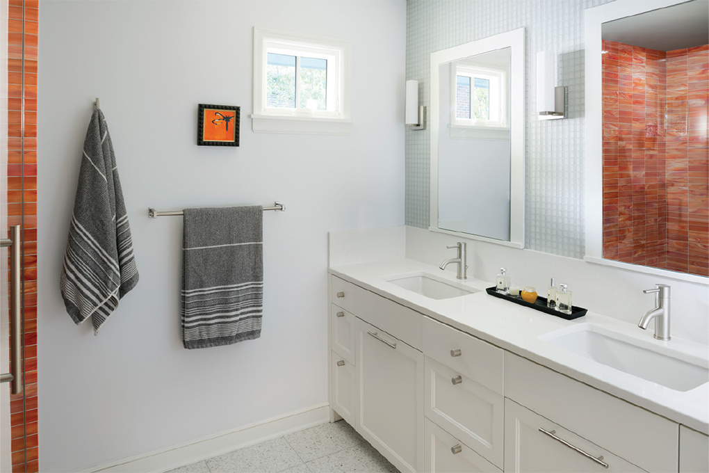 An all white bathroom pops with orange, glass tiles in the shower.