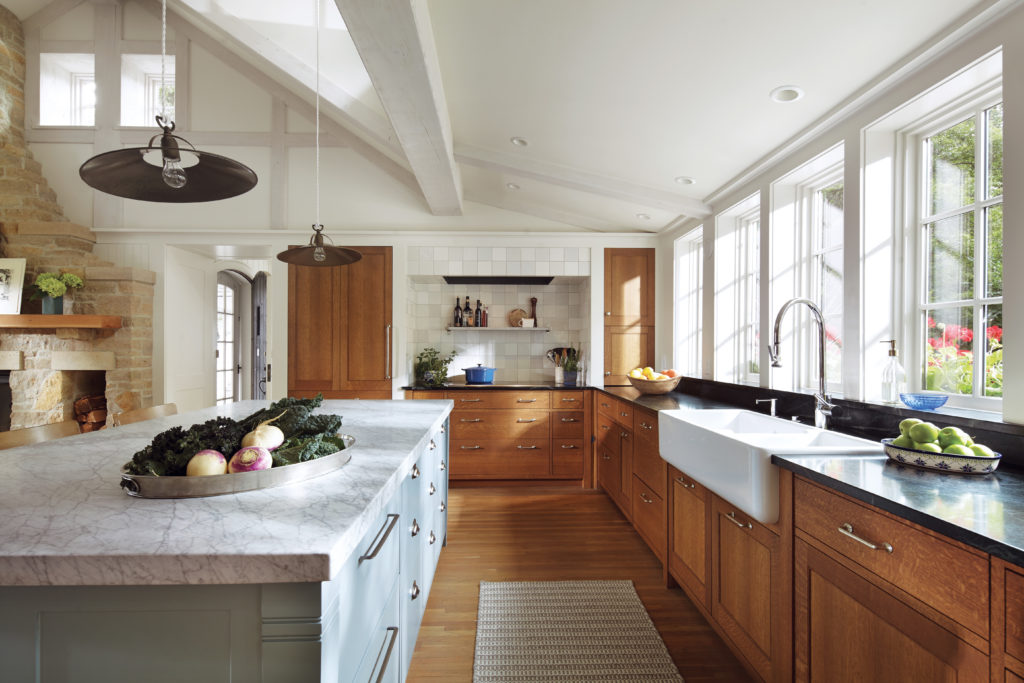 A kitchen in a remodeled home by Albertsson Hansen Architecture features matte-finished quarter-sawn oak cabinets, a farmhouse sink, and a large marble-topped island.