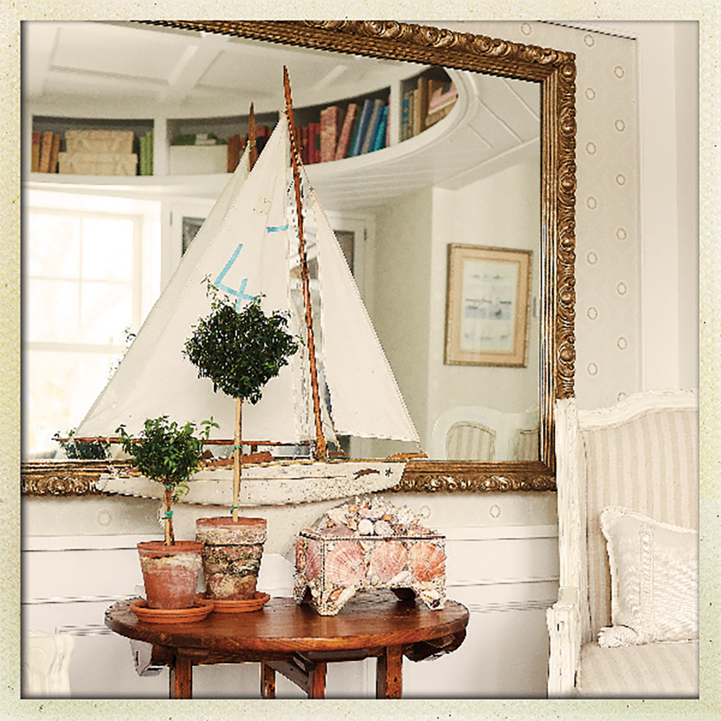 An antique model sailboat rests of a table with a circular bookshelf built into the ceiling above.