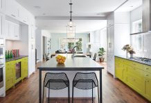 A kitchen with bold white and green cabinetry features a center island with surrounding chairs.
