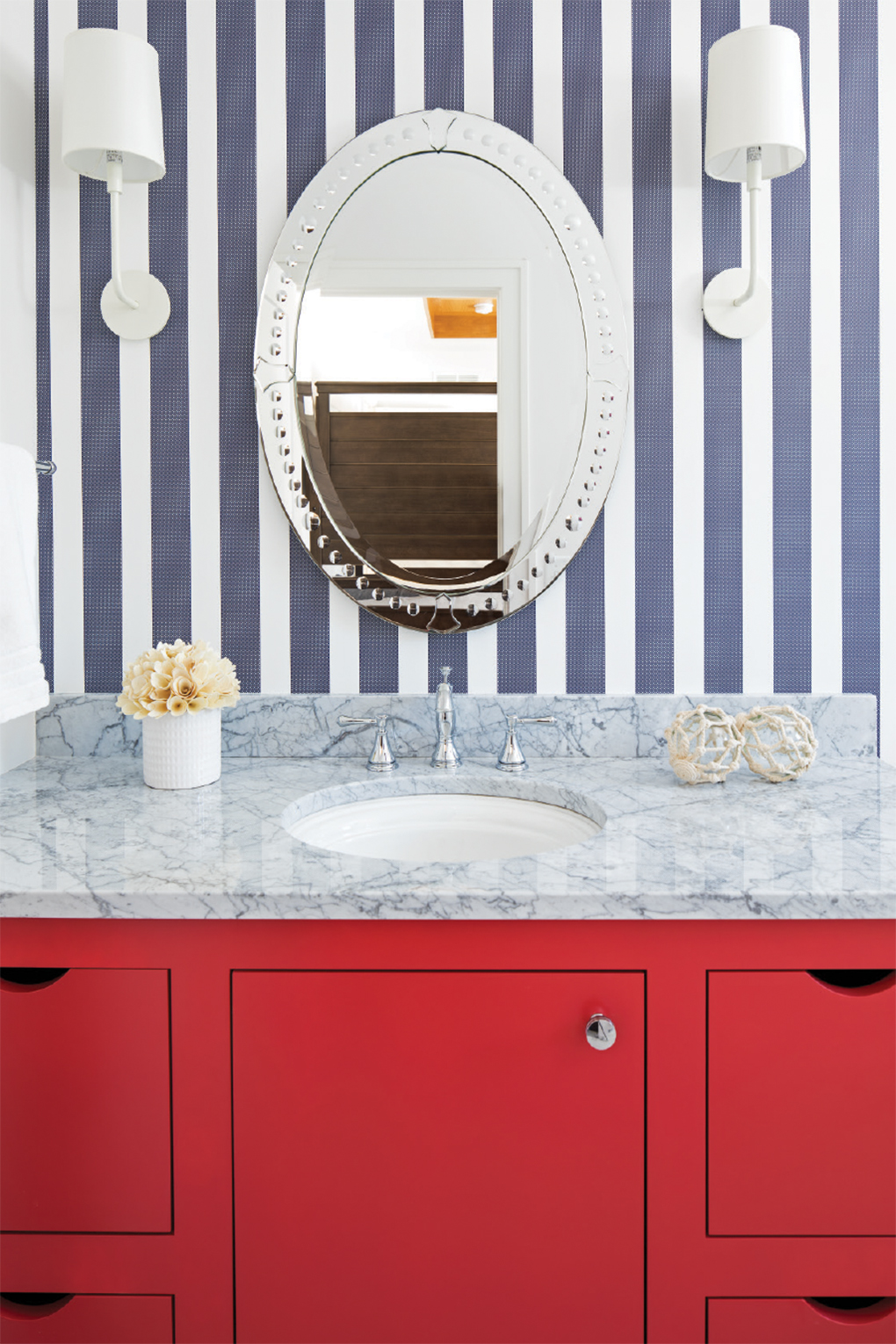 A bathroom with a red vanity and blue-striped wallpaper.