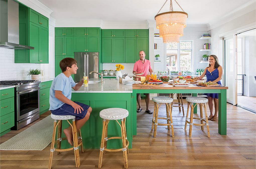 A family enjoying snacks in their kitchen with green cabinetry and, stainless steel appliances and white subway tile.