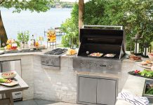 An outdoor kitchen with stainless steel grill, plates of food, and a table.