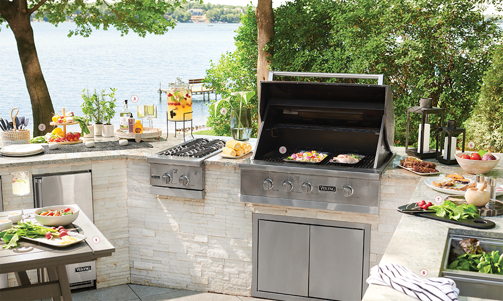 An outdoor kitchen with stainless steel grill, plates of food, and a table.