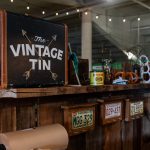 Part of Vintage Tin's store front. Wood counter, their logo, and more antique, original trinkets