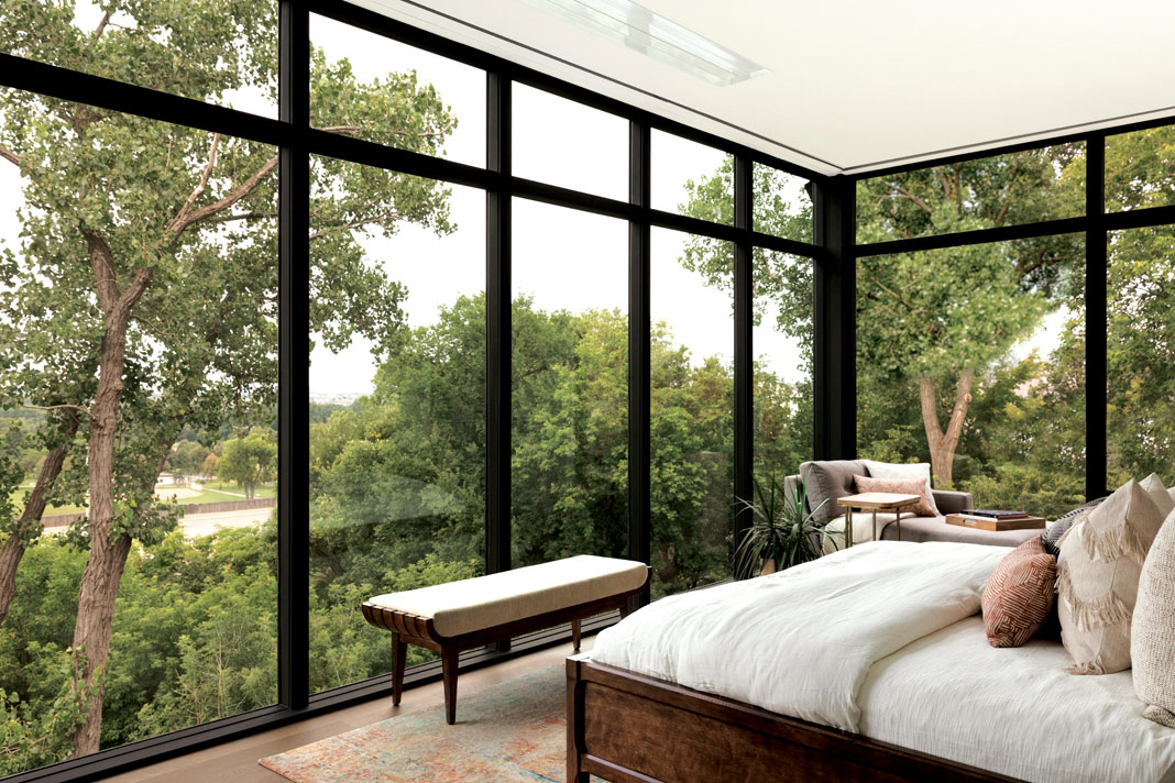 Floor-to-ceiling windows (equipped with retractable shades) in the master bedroom allow for a stunning panoramic view of the surrounding treetops, with glimpses of the Minneapolis skyline visible through the leaves. Part of Midwest Home's 2018 Luxury Home Tour.