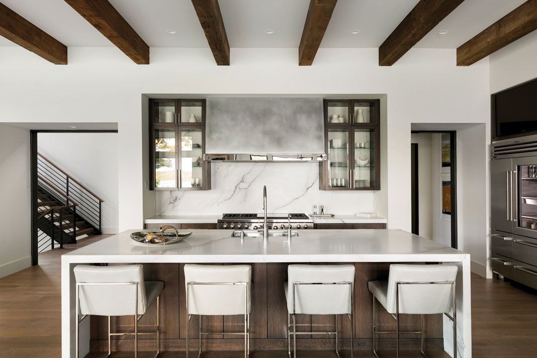 Dark wood flooring, ceiling beams, and custom oak cabinets add warmth to the kitchen, which features marble countertops and open access to the dining and gathering spaces. Part of Midwest Home's 2018 Luxury Home Tour.