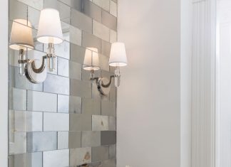 A bathroom with mirrored tiles, white sink and wall sconce light.