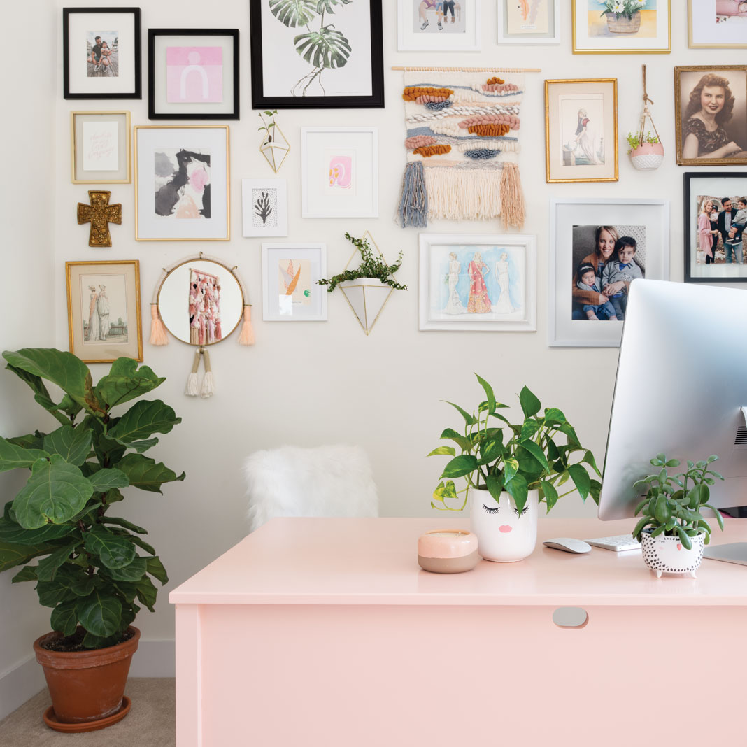 A wall full of framed photos and a pink desk with computer on top inside the office Jen Biswas, owner of Paisley + Sparrow.