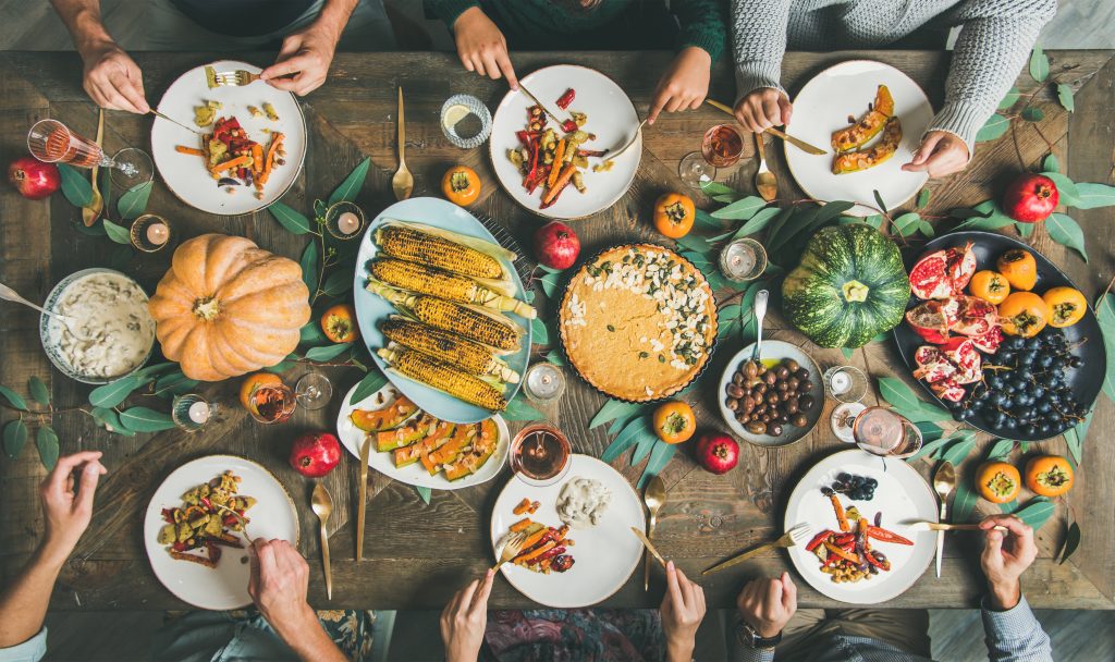 Vegan or vegetarian Thanksgiving, Friendsgiving holiday celebration. Flat-lay of friends eating meals at Thanksgiving Day table with pumpkin pie, roasted vegetables, fruit, rose wine, top view